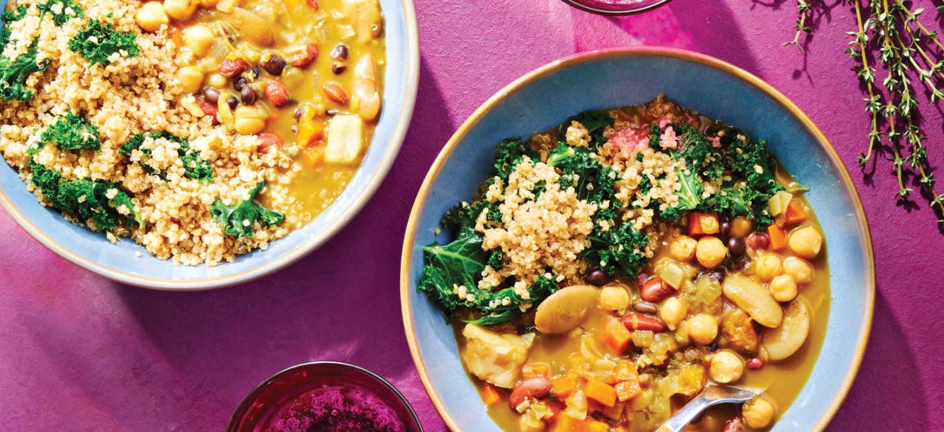 Two bowls of 4-Bean Jamaican Ital Stew with Herbed Quinoa and Kale on a dark pink background with a few sprigs of time