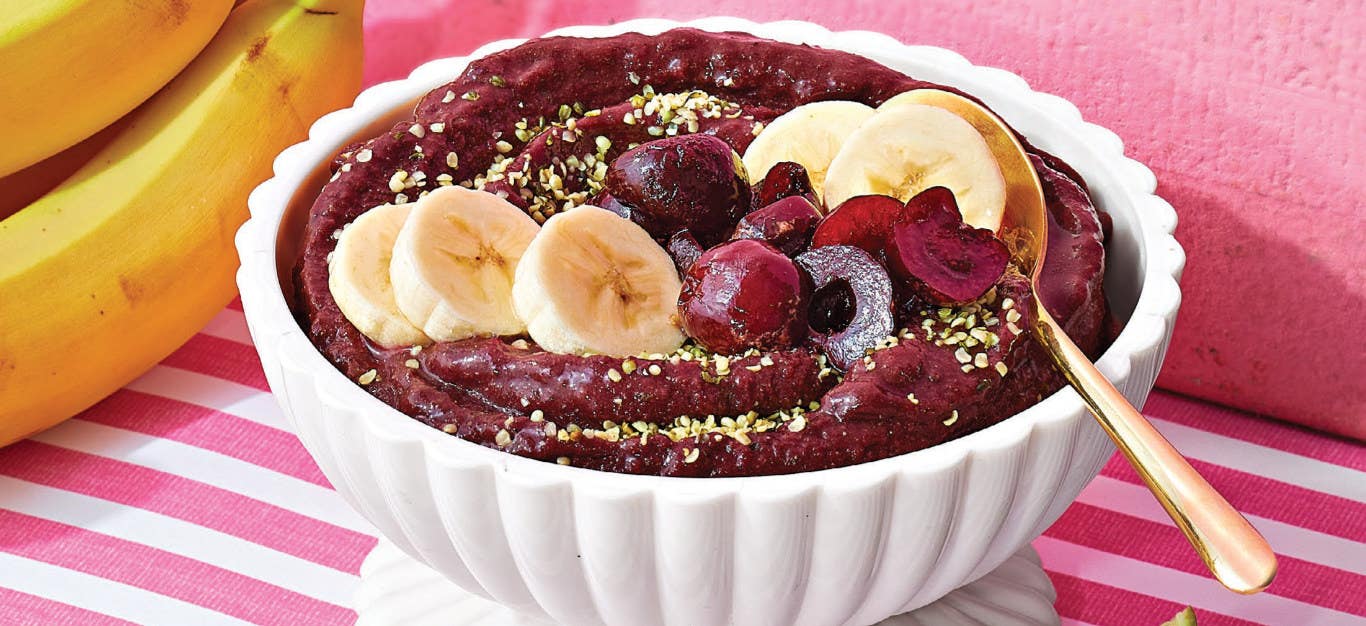 Cherry and Acai Smoothie in a white bowl on a pink and white striped tablecloth next to a couple of bananas