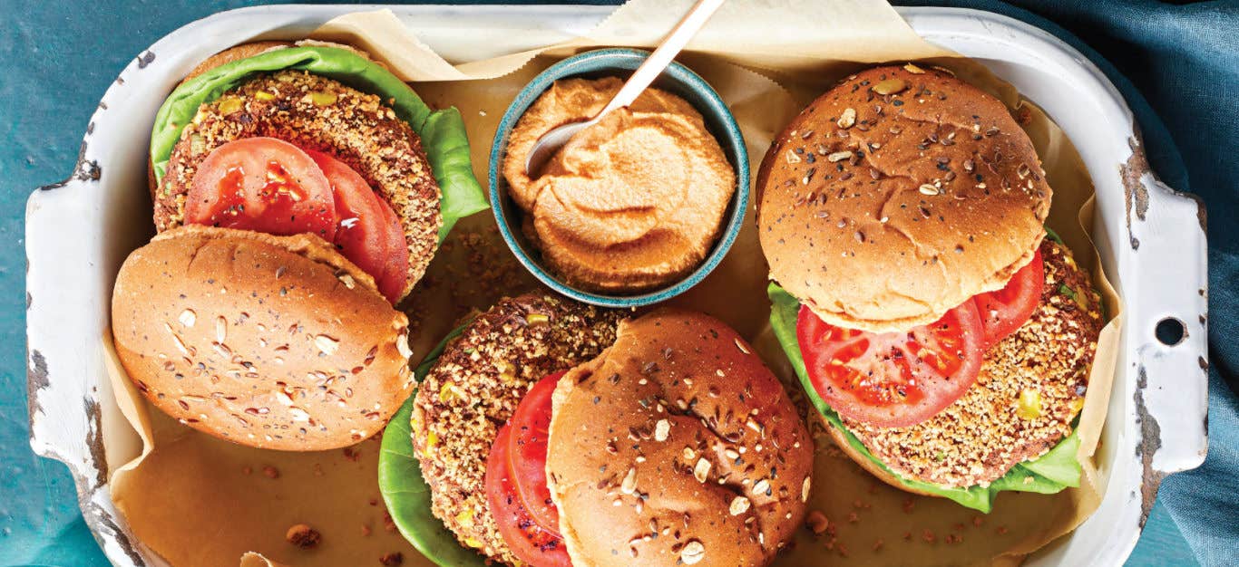 Three Chipotle-Lime Black Bean and Jackfruit Burgers in a white enamel pan with a small pot of chipotle-lime sauce.