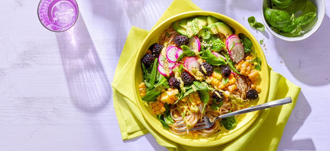 Easy Gourmet Noodle Bowls with Blackberries, Fresh Corn, and Avocado-Lime Dressing on a yellow cloth napkin against a lilac background