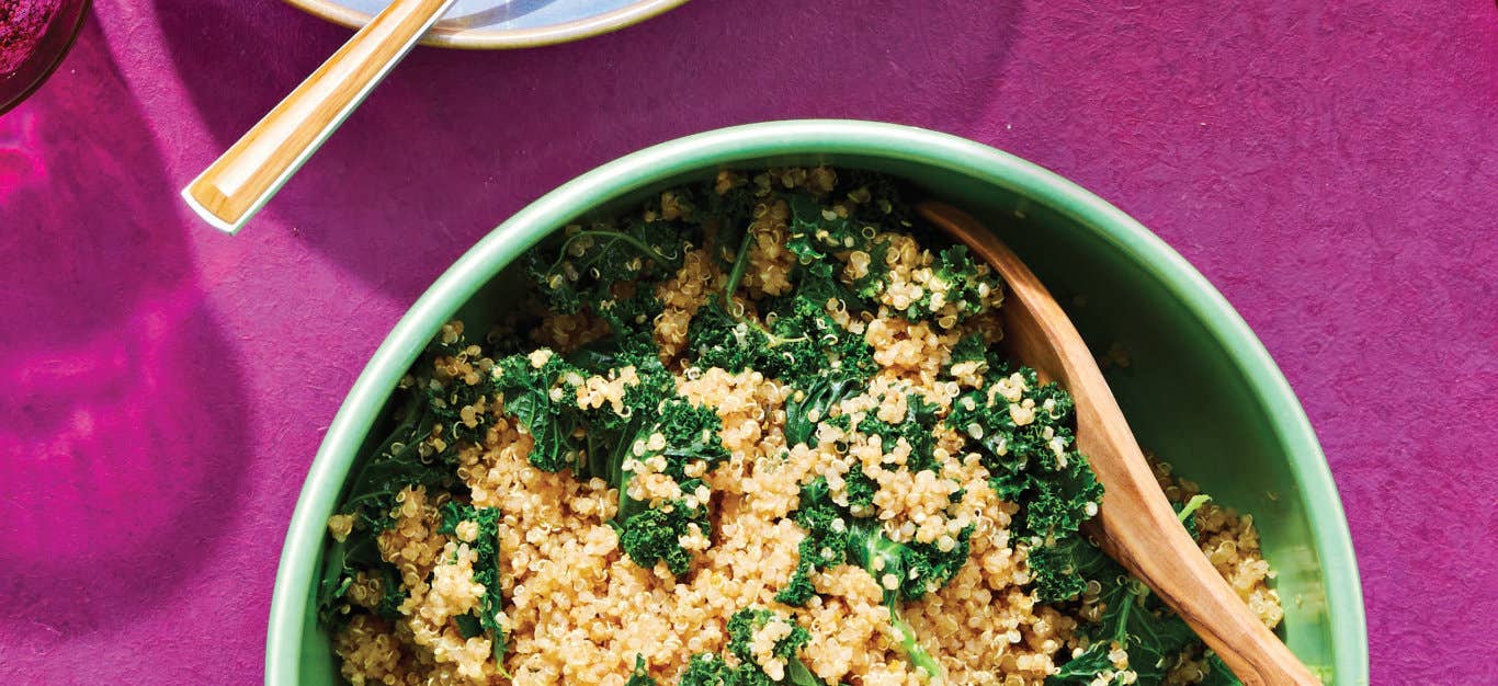 Herbed Quinoa with Kale in a green bowl with a wooden spoon against a bright pink background