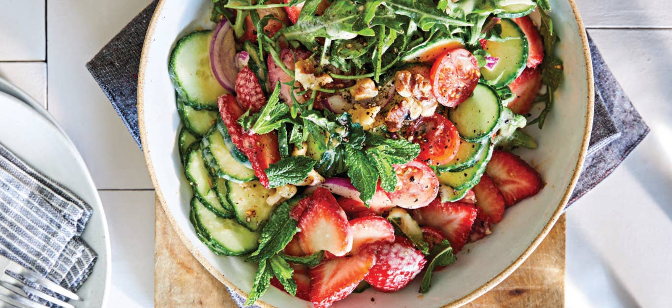 10-Minute Strawberry Cucumber Salad in a white ceramic bowl on a wooden chopping board and a blue cloth napkin