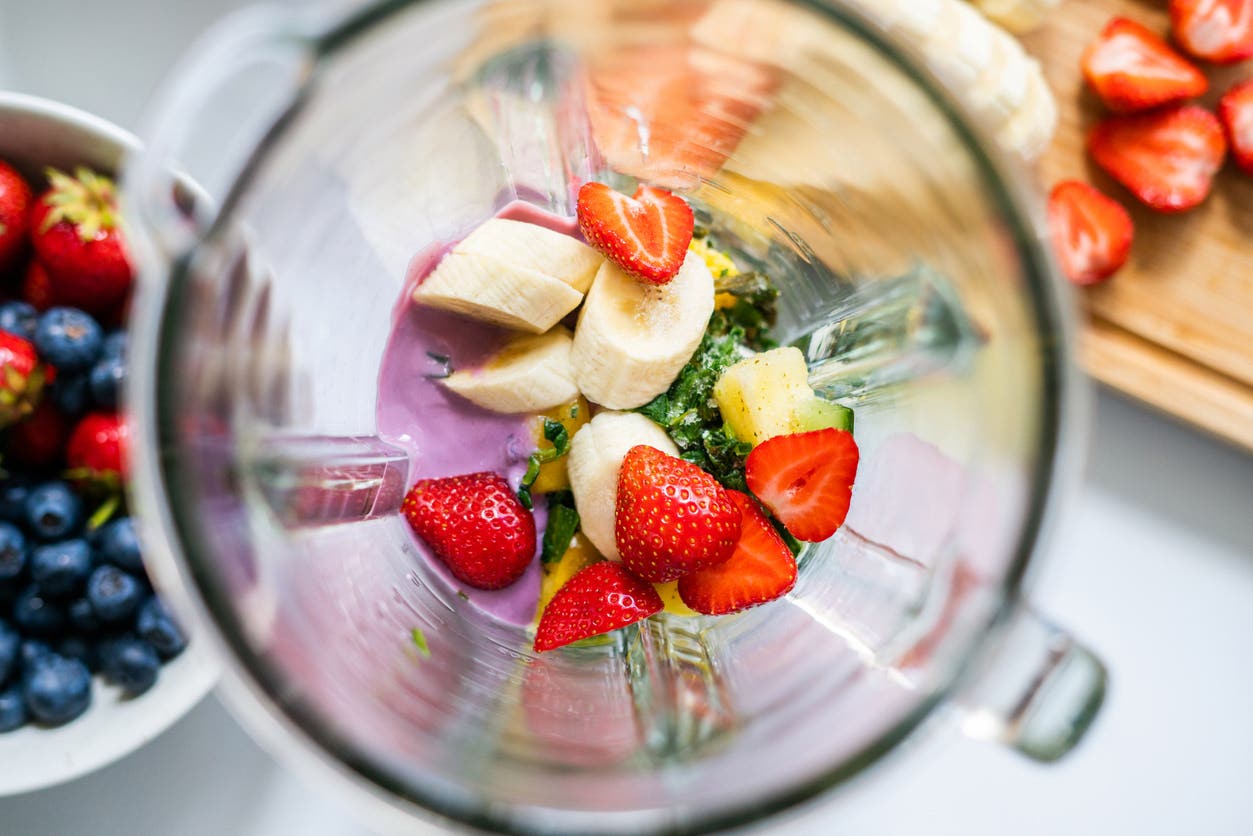 Top-down view into a blender with fruit smoothie ingredients inside of it