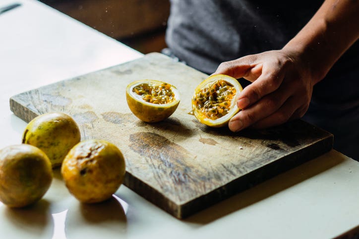 Hand of an unrecognizable person cutting passion fruit on a board.