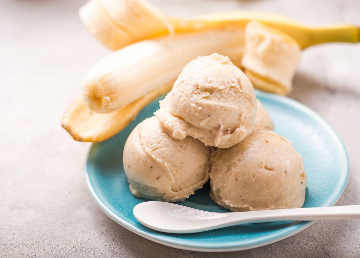 three scoops of nice cream (ice cream made from frozen bananas) on a plate with a spoon, with a banana visible in the background