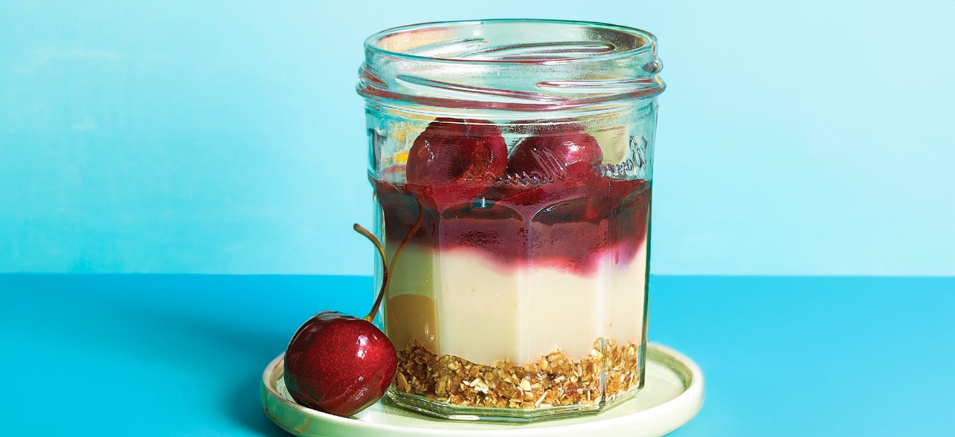 Mini Cherry Panna Cotta Parfaits on a small white plate with a fresh cherry on the side of the plate against a pale blue background