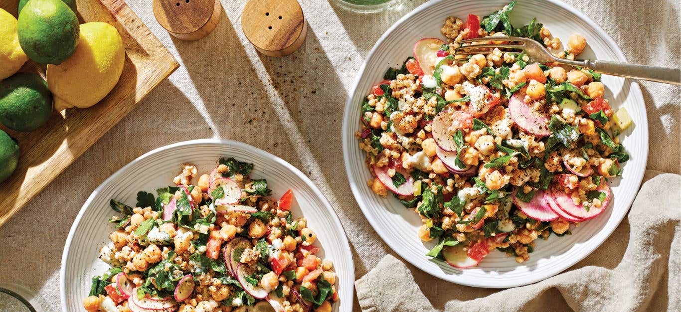 Two bowls of Buckwheat Tabbouleh with Chard, Chickpeas, and Creamy Garlic Dressing on a cream background with a fork in one of the bowls