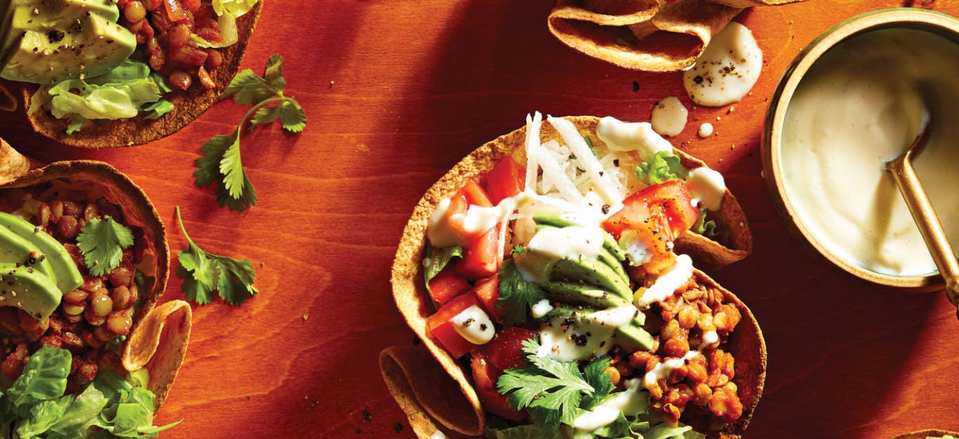 Lentil Taco Salad in Crispy Tortilla Bowls on a red tabletop next to a small bowl of lime crema