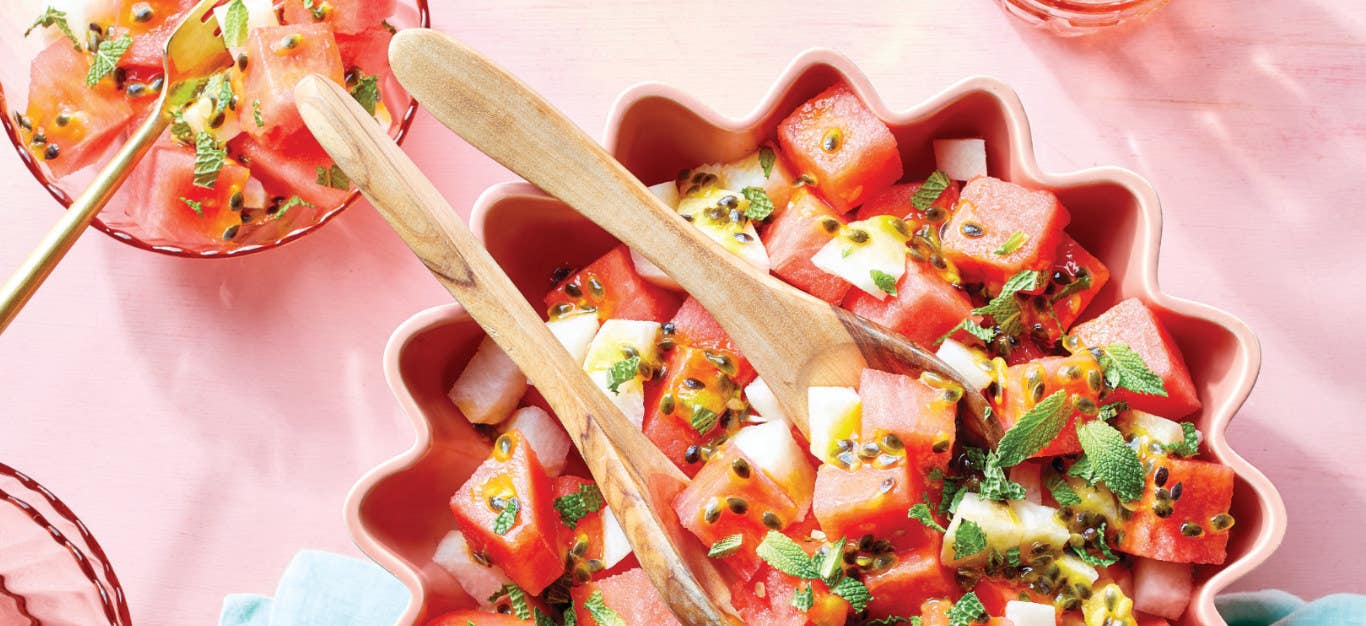 Watermelon Salad with Passion Fruit Dressing in a pink bowl on a pink background with wooden serving spoons in the bowl