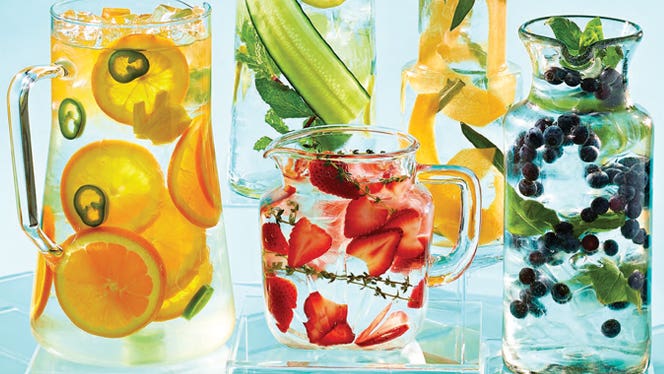 Four different vessels with fruit infused water - one with orange slices, one with strawberry slices, one with cucumber slices and herbs, and one with lemon