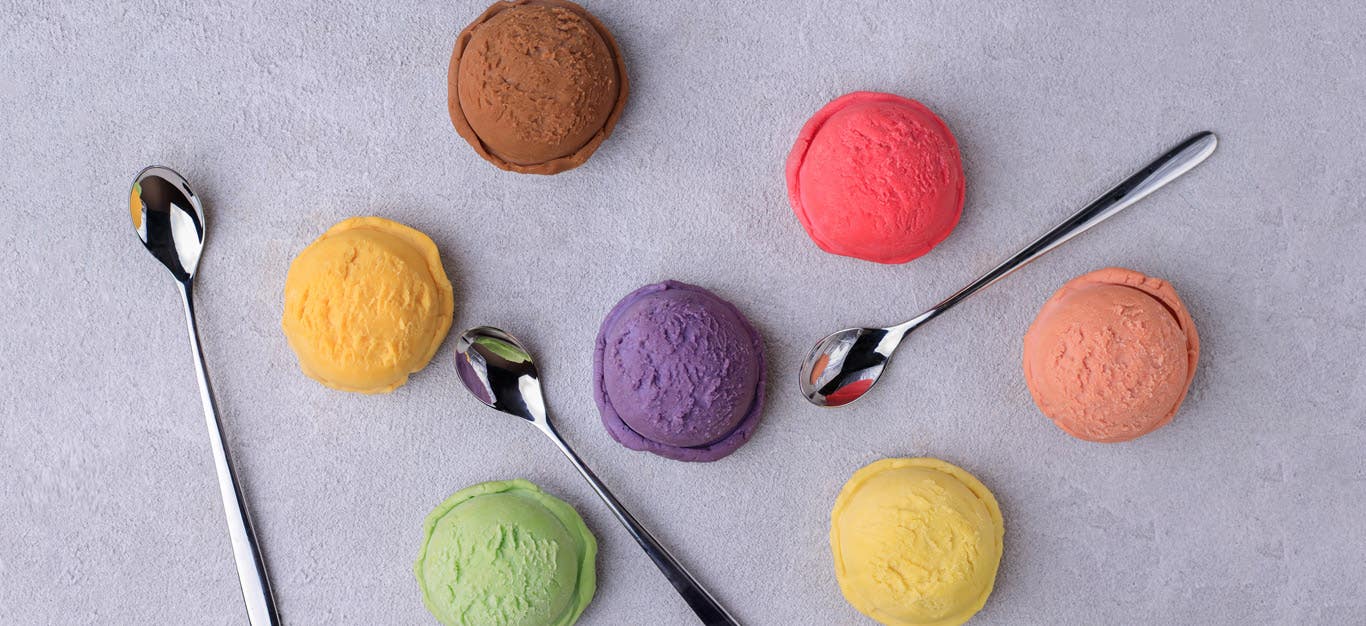 Colorful individual scoops of ice cream on a light purple surface, with spoons next to them