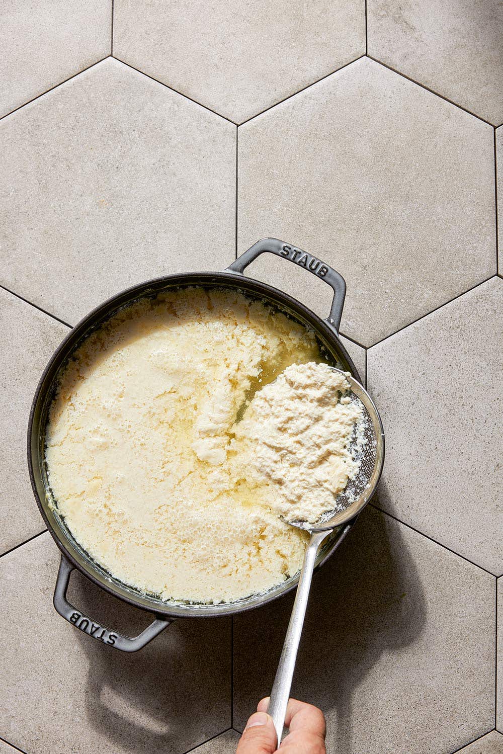 homemade soy bean curd in a pot, with a large spoon scooping up some of the solid parts for making tofu