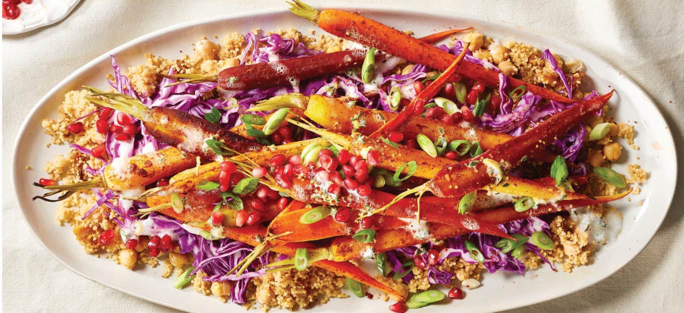 A large white platter of Harissa Roasted Carrot Salad with Couscous on a white table cloth