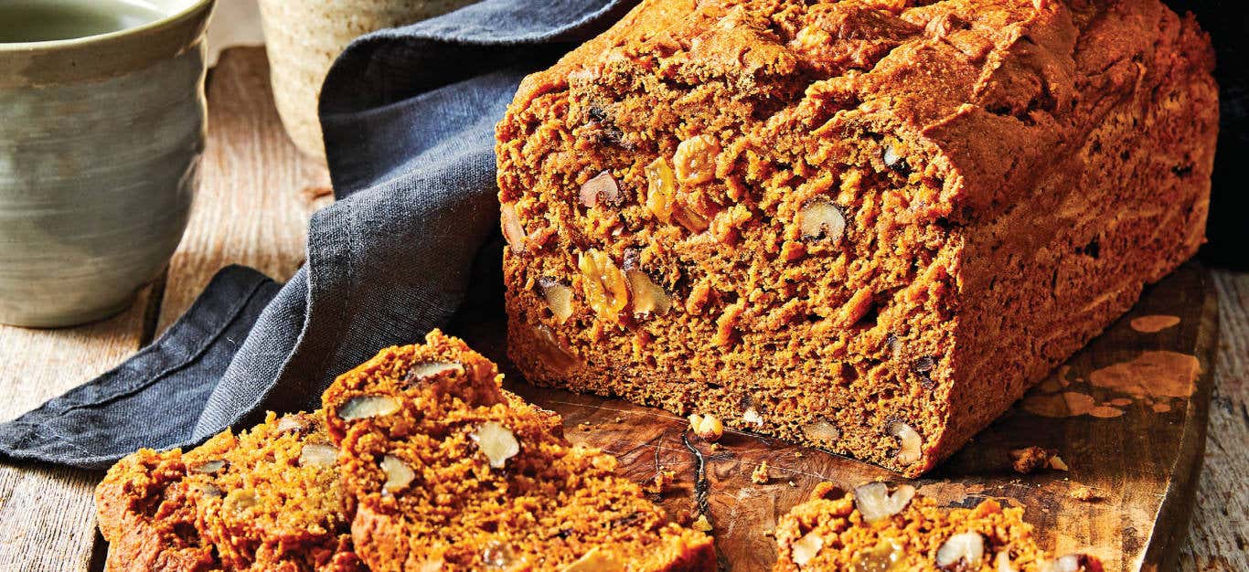 Pumpkin Spice Bread on a wooding chopping board, with a couple of slices cut, sitting in front of the loaf