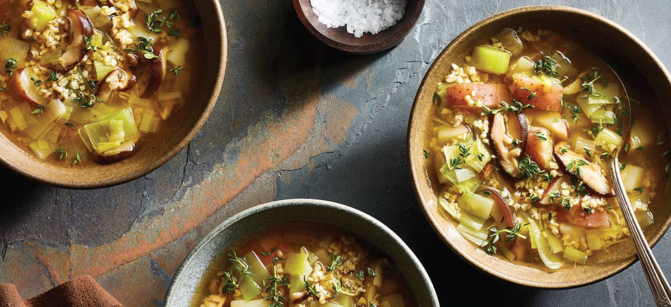 3 Bowls of 8-Ingredient Leek and Mushroom Soup sitting on a granite counter next to a small bowl of coarsely ground sea salt