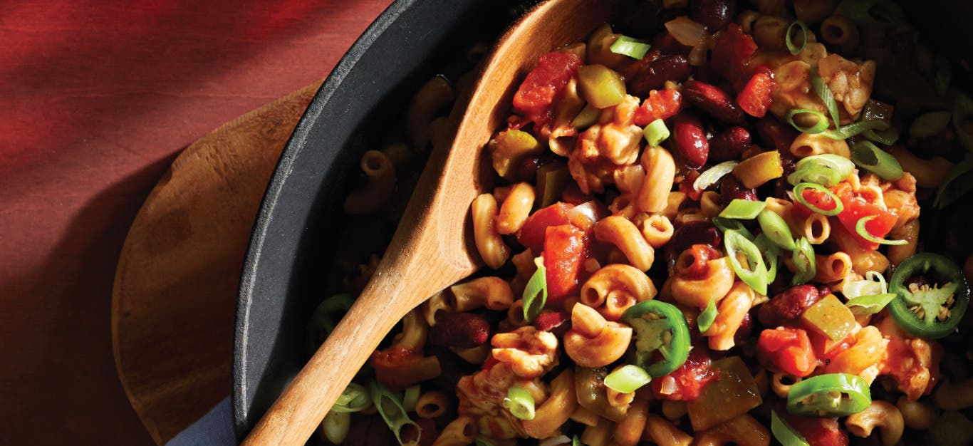 A skillet of One-Pot Spicy Tempeh Chili Mac with a wooden spoon