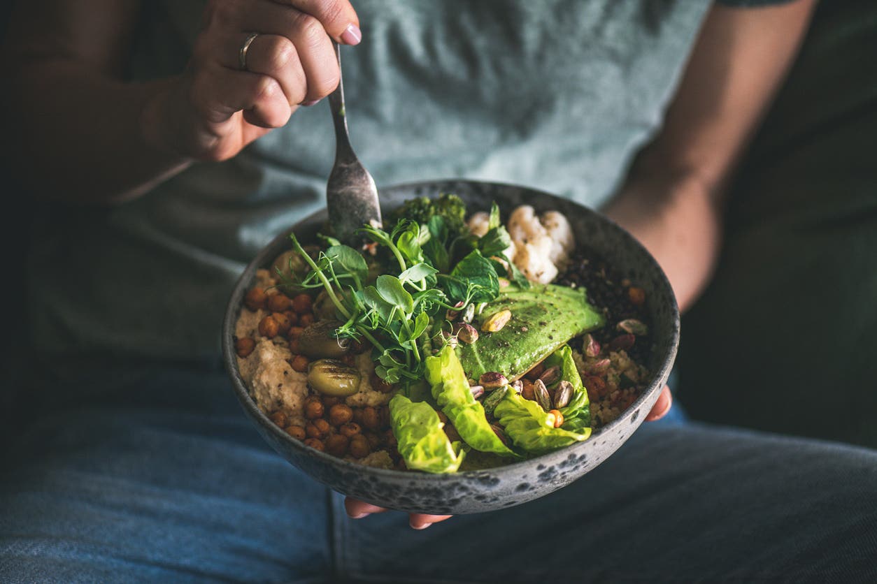 person eating a healthy vegan bowl meal featuring hummus, vegetable, salad, beans, couscous and avocado