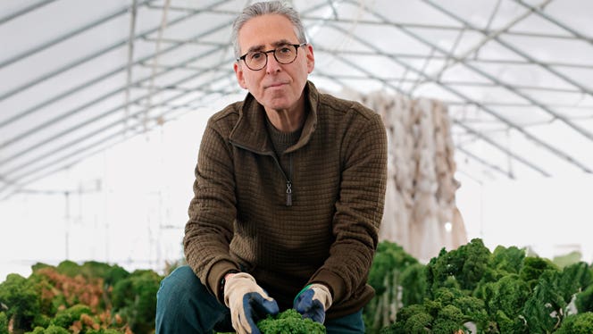 Dr. Ron Weiss, founder of Ethos Farm to Health, works in a greenhouse holding a cruciferous vegetable that he's grown