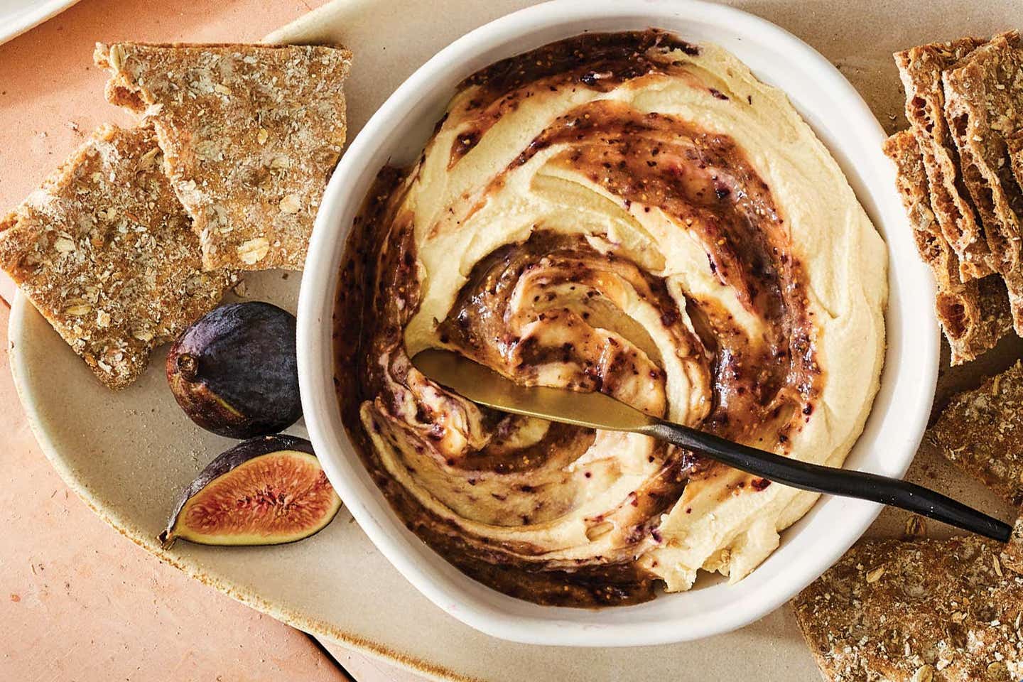 Hummus with a fresh fig paste swirled into it, next to some whole grain crackers