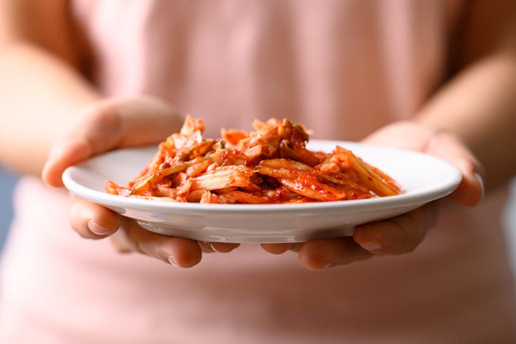 Hands holding a plate of fermented kimchi