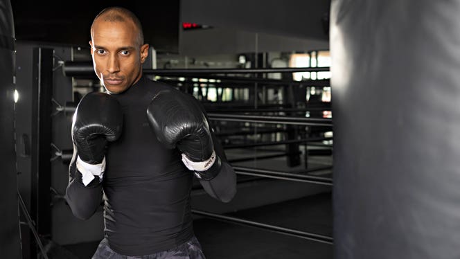 Boxer and celebrity trainer Kollins Ezekh poses in a gym wearing boxing gloves holding up his hands