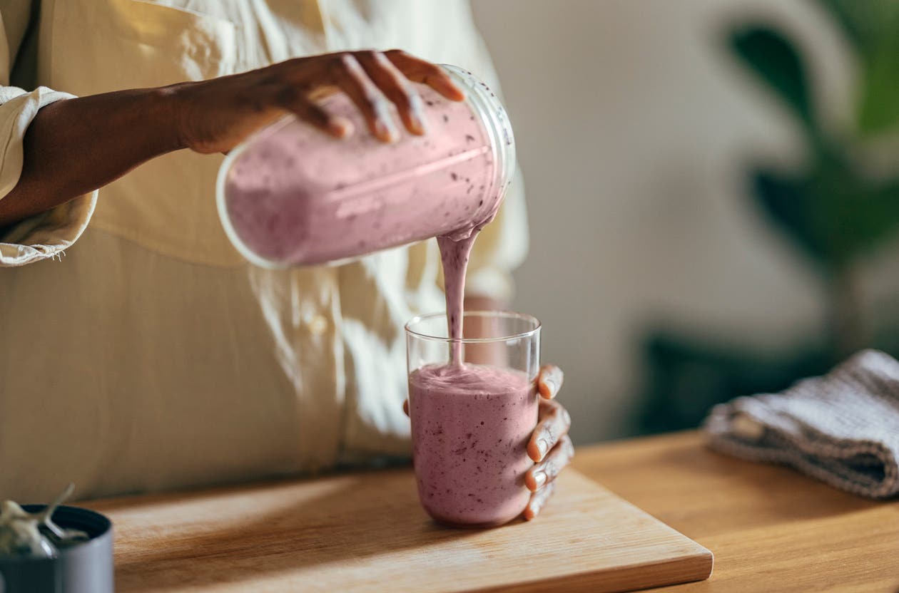 A woman pours a berry smoothie from a blender pitcher into a glass