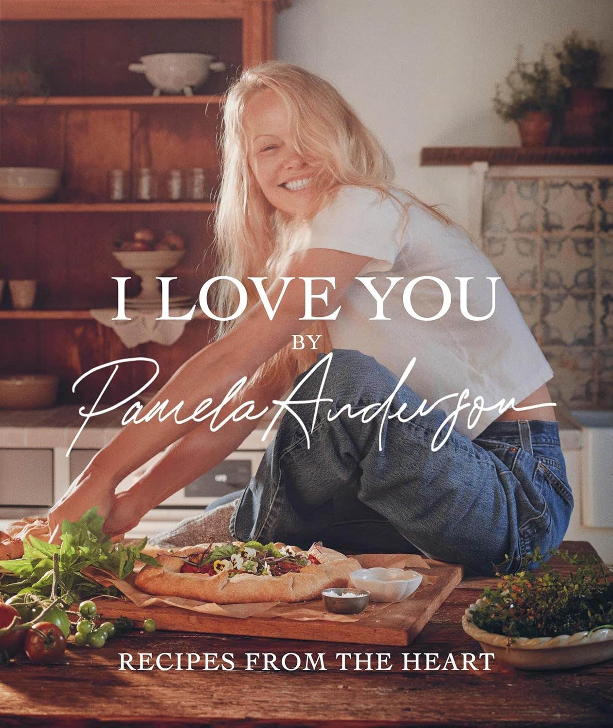 Cover of Pamela Anderson's cookbook I Love You, showing Pam Anderson sitting on a counter in jeans and a white shirt