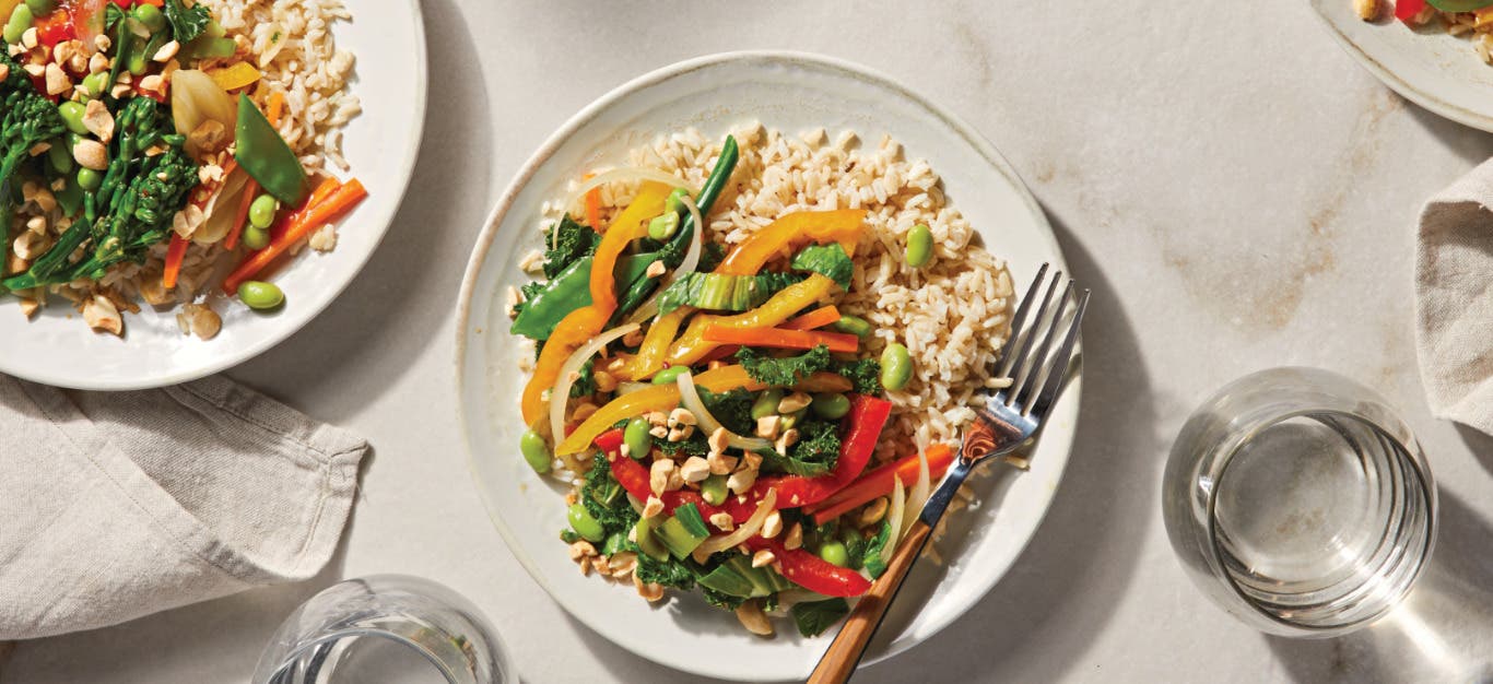 Low-Salt Veggie Stir-Fry over brown rice on two white dinner plates with a fork resting on the side of the plate