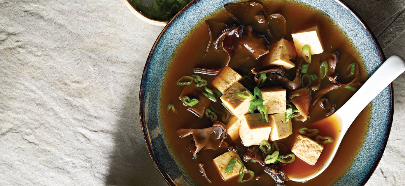 Chinese Hot and Sour Soup with Tofu in a blue ceramic bowl with a white spoon in the bowl