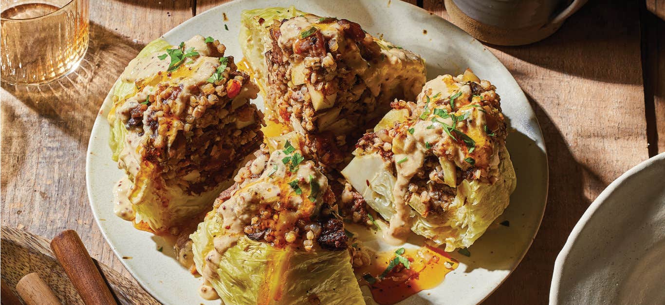 Stuffed Whole Cabbage with Kasha cut into quarters on a white plate, drizzle with Mustard Cream and Apple Cider Reduction