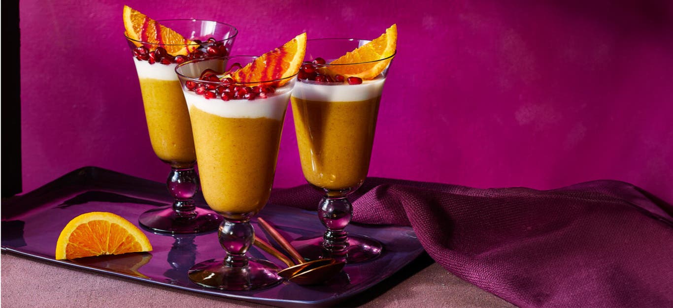 Jamaican Orange Cornmeal Pudding with Coconut Fluff in parfait glasses served with a wedge of orange and pomegranate seeds