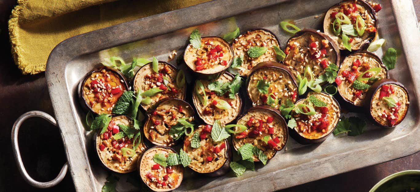 Vietnamese Eggplant with Cashews, Sesame, and Chile cut into 16 rounds, presented in a metal baking tray garnished with fresh mint leaves