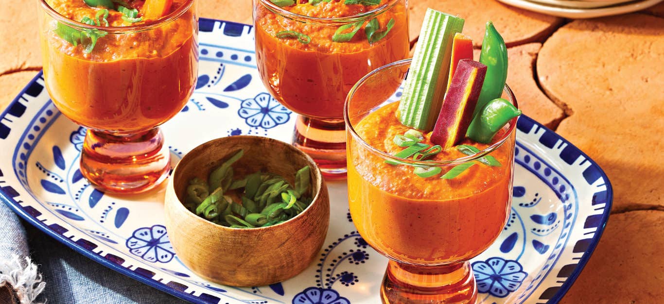 Three servings of Spicy Buffalo Hummus serve in glass glasses with a sturdy stem, with veggies sticks sticking out of them