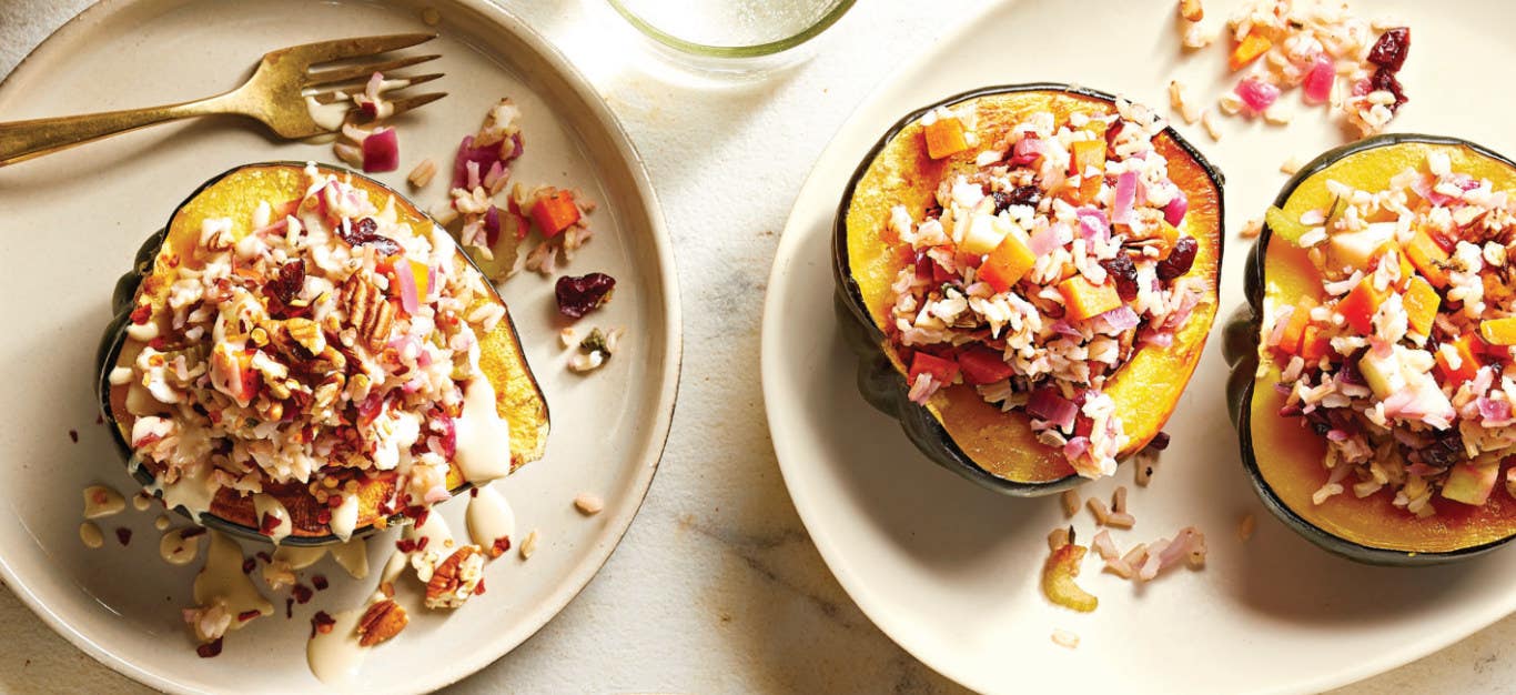 one Vegan Stuffed Acorn Squash half on a plate, drizzle with Creamy Tahini Sauce and fork on the side, next to a serving plate with two halves