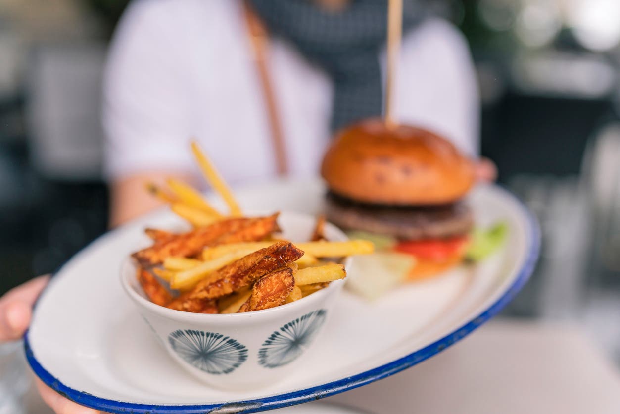 person holding out burger and deep-fried french fries on a plate