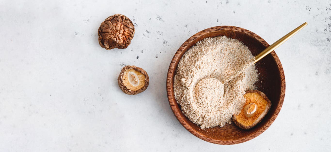 a top-down shot of a bowl of ground shiitake mushroom powder aka shroomami dust, an umami-rich salt-free seasoning you can make at home, shown beside a few dried shiitake on a marble counter