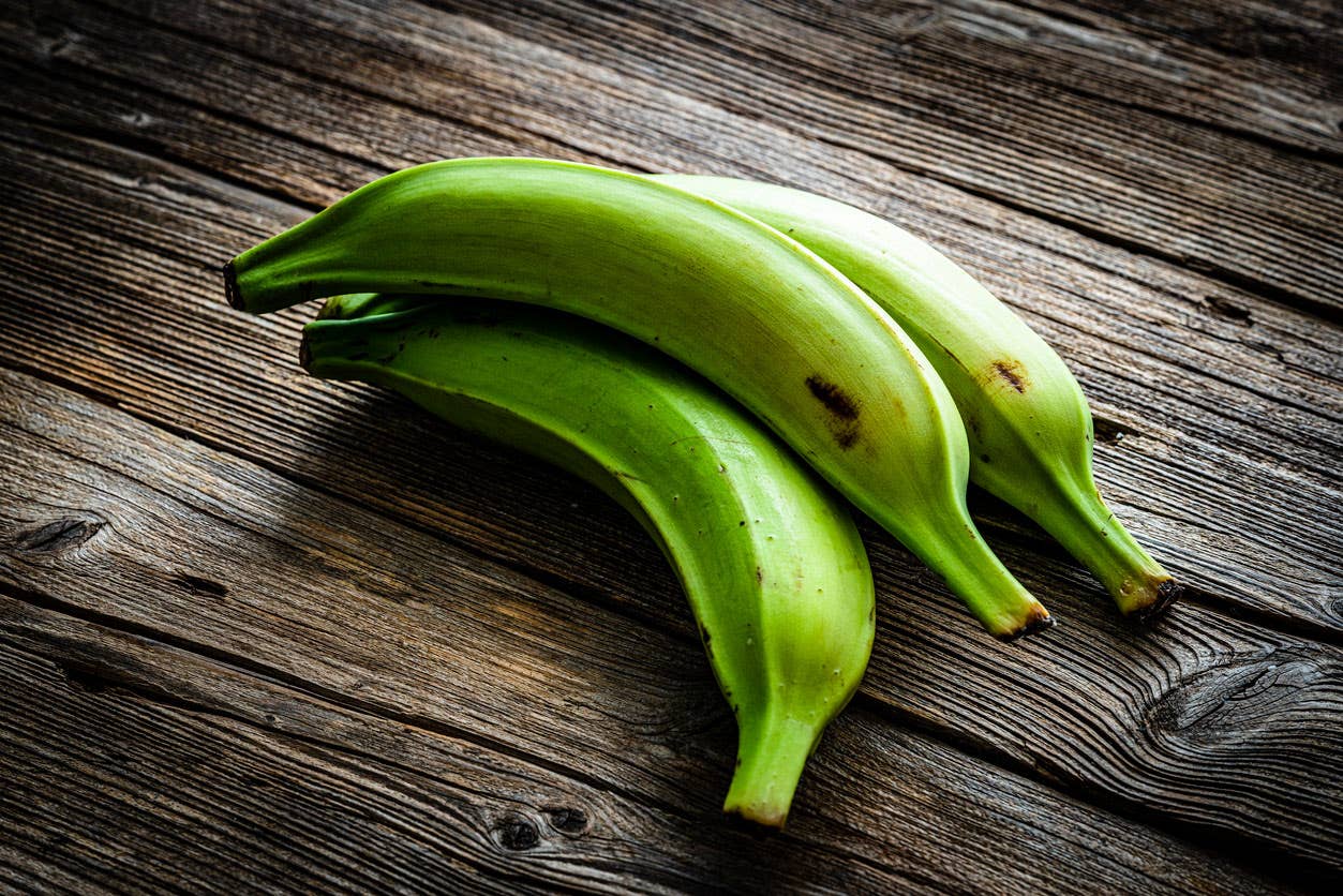 three green unripe plantains on a rustic wooden surface