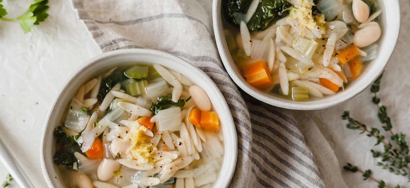 Two bowls of whole wheat orzo pasta soup with cannellini beans and kale