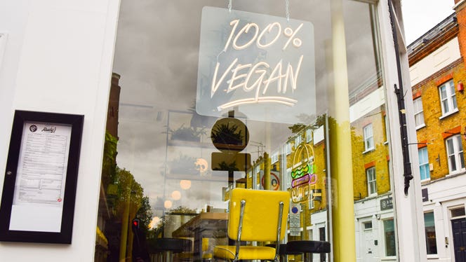 A restaurant window with a neon sign that says "100% VEGAN"