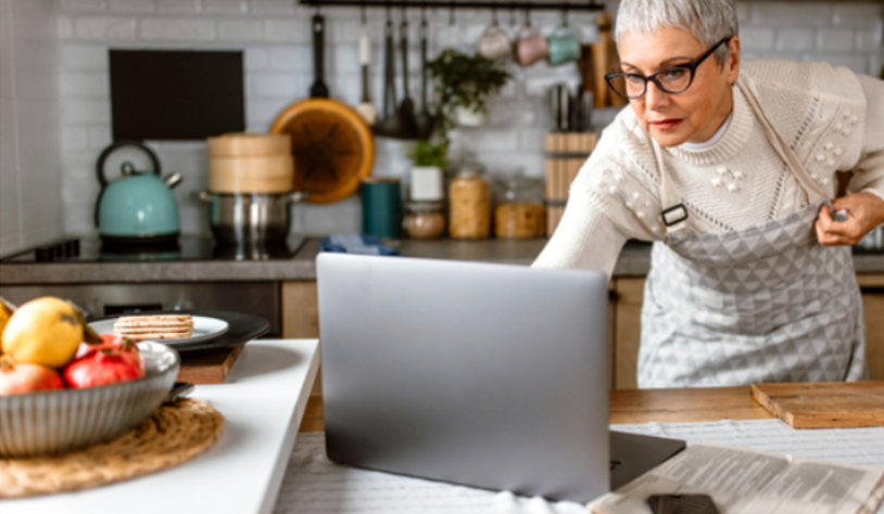 Older woman in the kitchen reading cooking instructions on her laptop