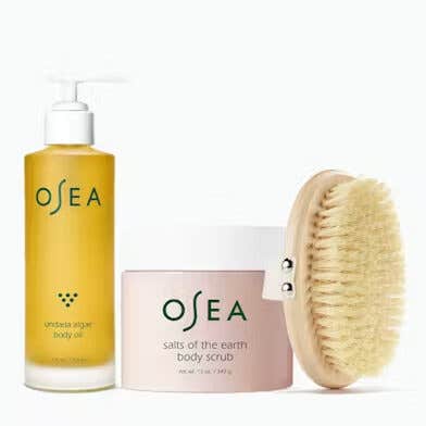 The Total Body Glow trio by Osea, featuring a body scrub, body oil, and body brush