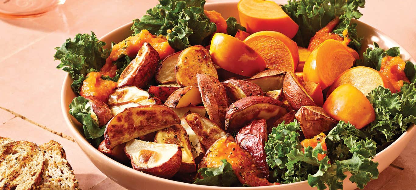 Warm Roasted Potato, Kale, and Persimmon Salad in a peach bowl on a peach counter