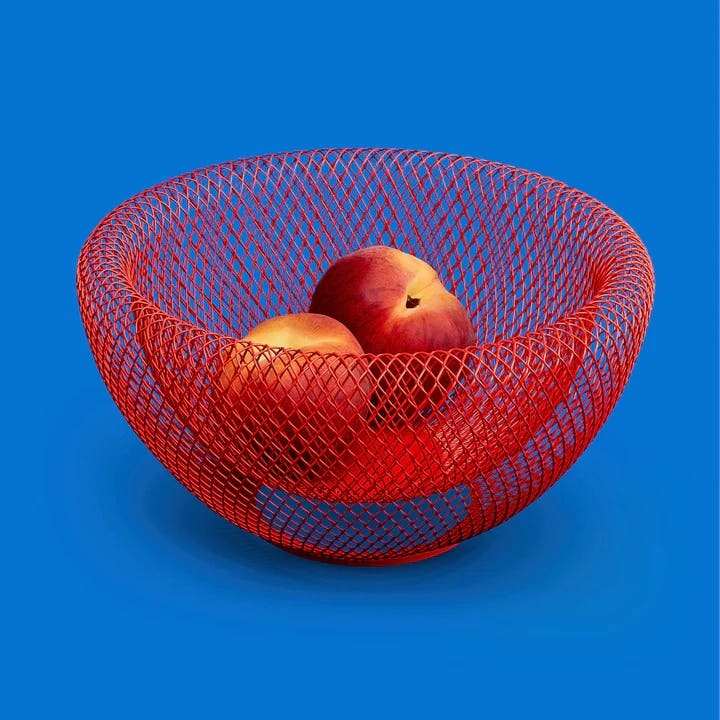 A red wire mesh fruit basket with two peaches inside it, shown on a blue background, from the Museum of Modern Art Design Store