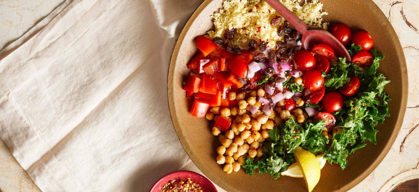 Lemony Moroccan Couscous Salad in a brown bowl with a wooden spoon on a cream-colored cloth napkin