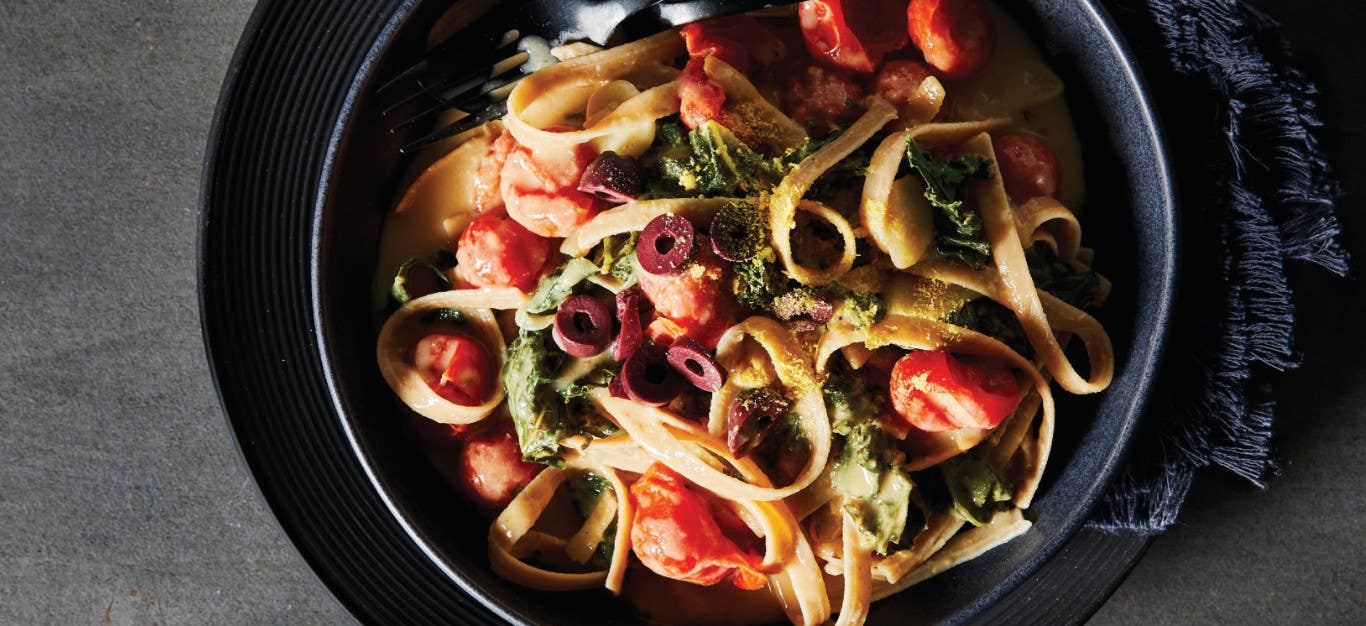 Creamy Baked Fettuccine with Kale in a black serving bowl on a black plate with a black cloth napkin