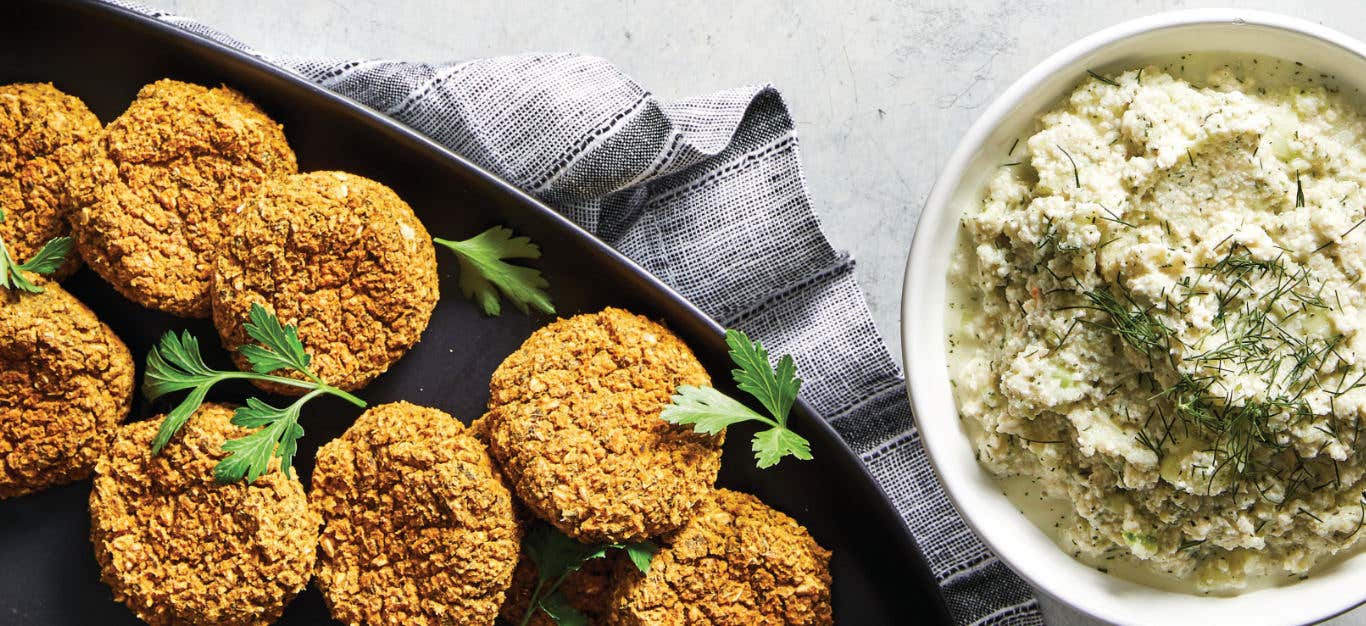 Baked Falafel in a black baking tray with a white bowl of Vegan Tzatziki Sauce to the side