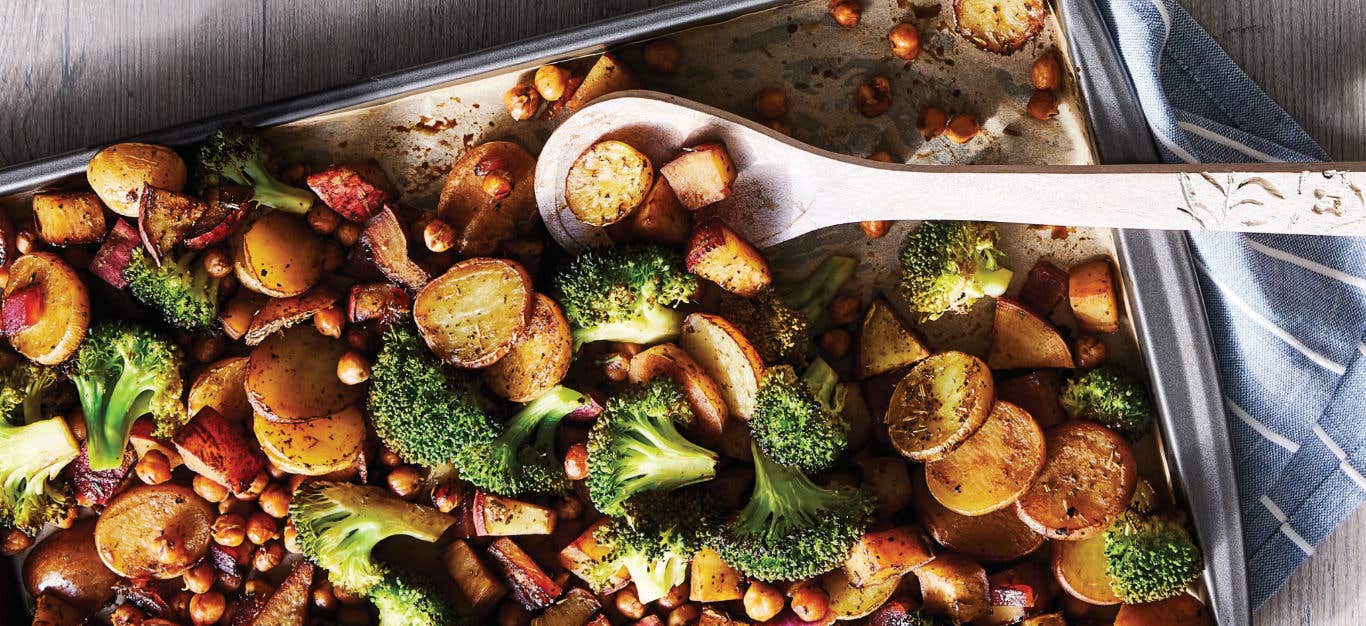 Sheet Pan Supper with Broccoli, Spuds, and Maple-Balsamic Chickpeas in a baking tray with a serving spoon resting in the pan