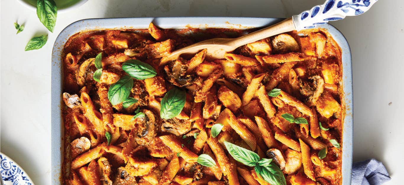 Mediterranean Pasta Bake with Mushrooms and Eggplant in a white and blue casserole dish with a serving spoon