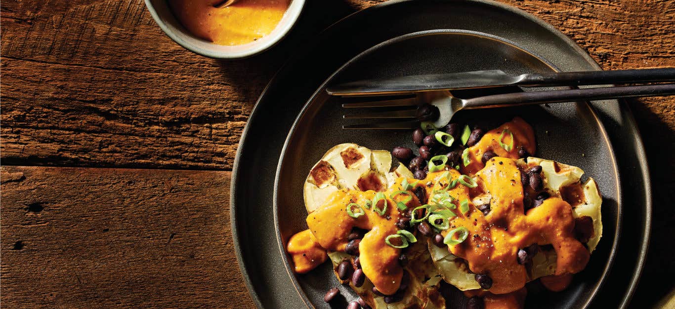 Easy Potato Waffles with Vegan Nacho Cheese Sauce on a black plate with a knife and fork and a small bowl of nacho cheese sauce off to the side