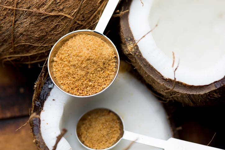 Coconut/palm sugar in measuring spoons with a coconut in the background